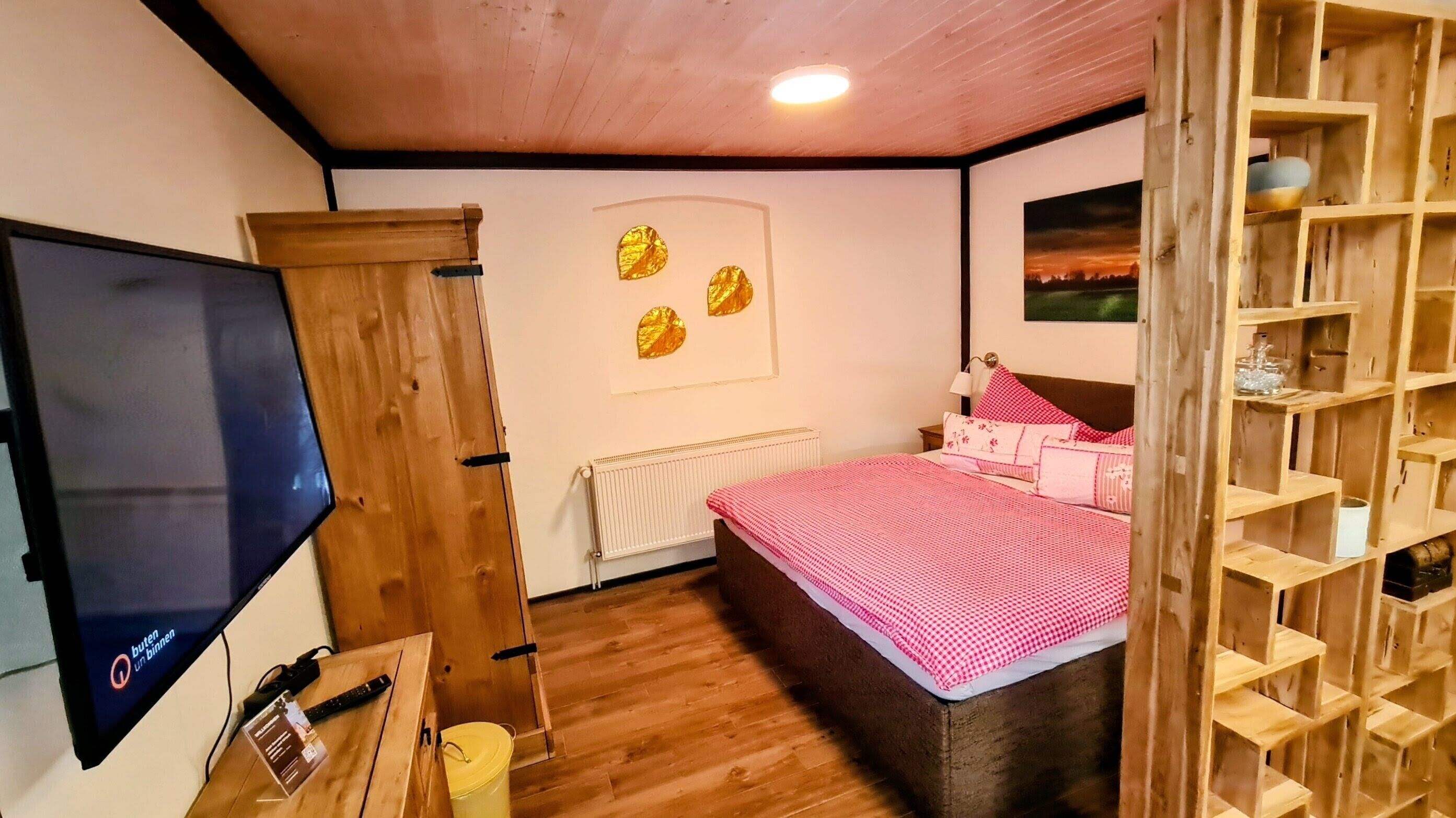 A bedroom with a bed, a television, a radiator, and a wooden shelf unit.
