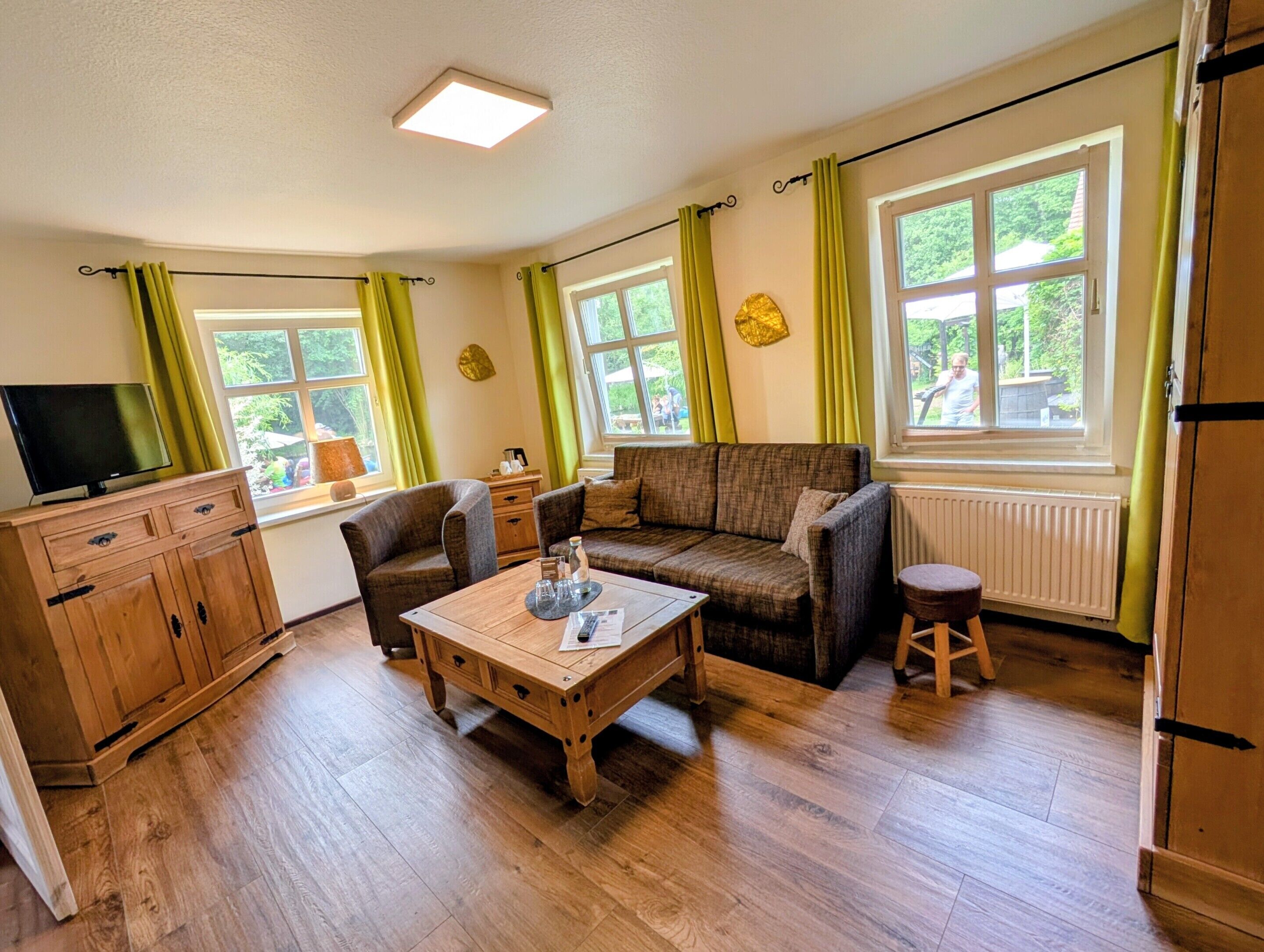 A cozy living room with a sofa, armchairs, a coffee table, a TV, and a wooden cabinet.