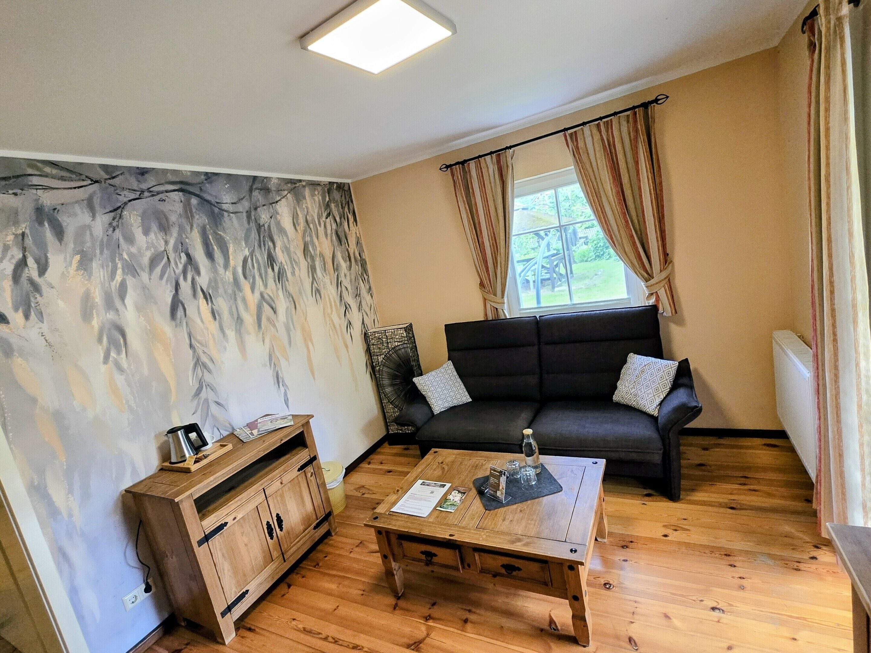 Ein gemütliches Wohnzimmer mit einer Couch, einem Holztisch und einer Wand mit Blätermotiv.