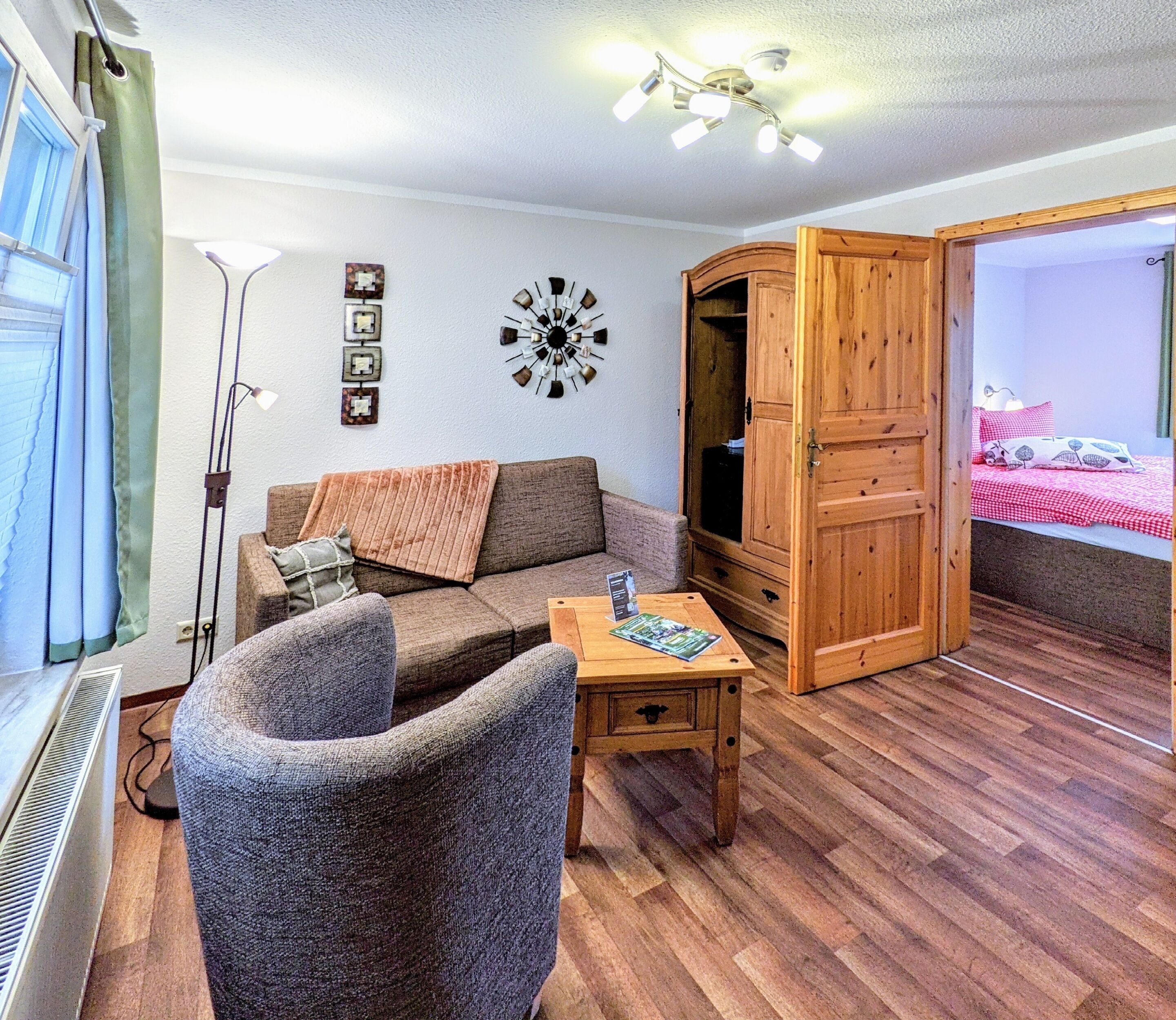 Una sala acogedora con sofá, sillón, aparador de madera y una mesa con una revista.