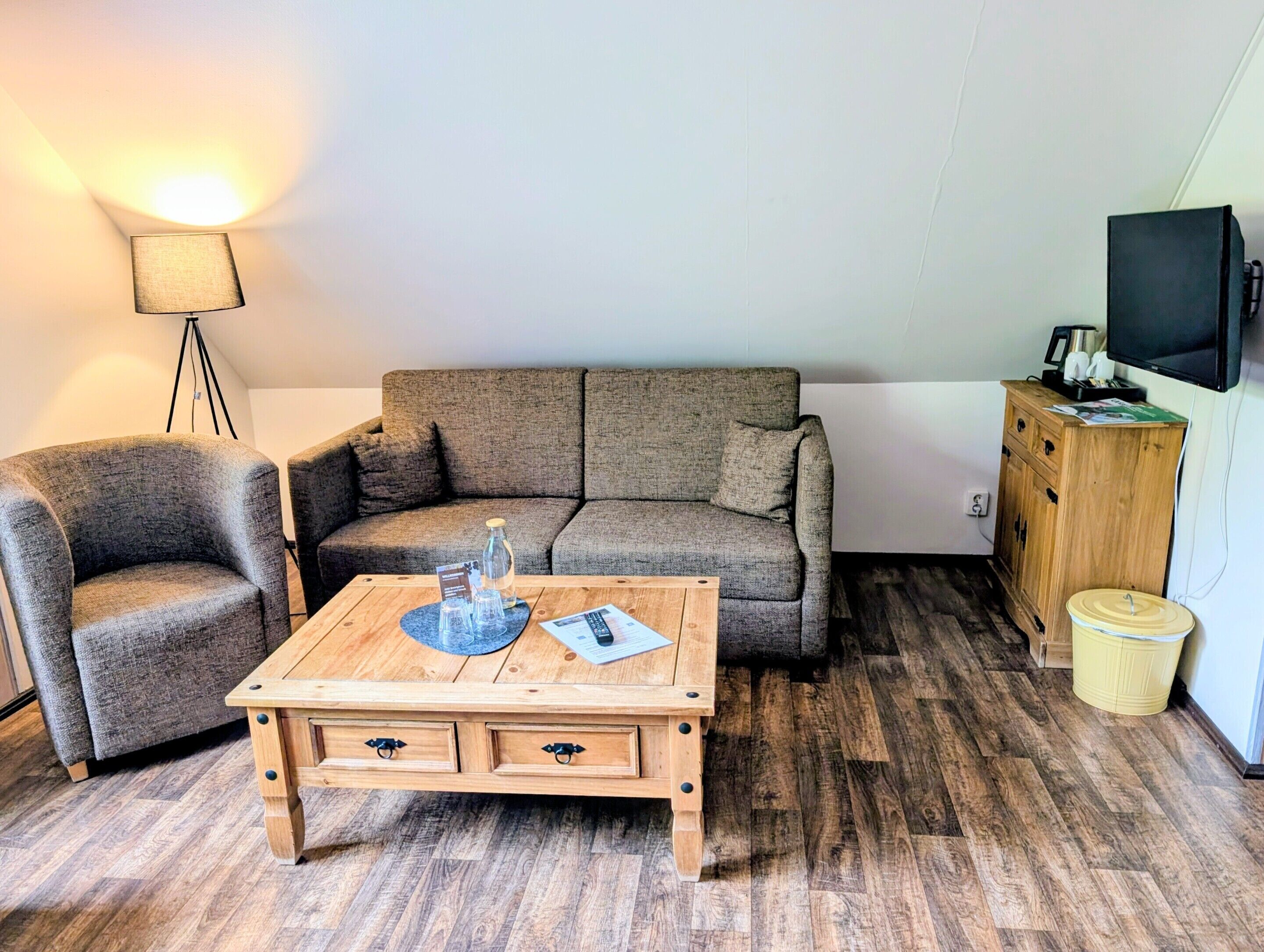 A living room with a sofa, armchair, coffee table, lamp, television, and wooden cabinet.