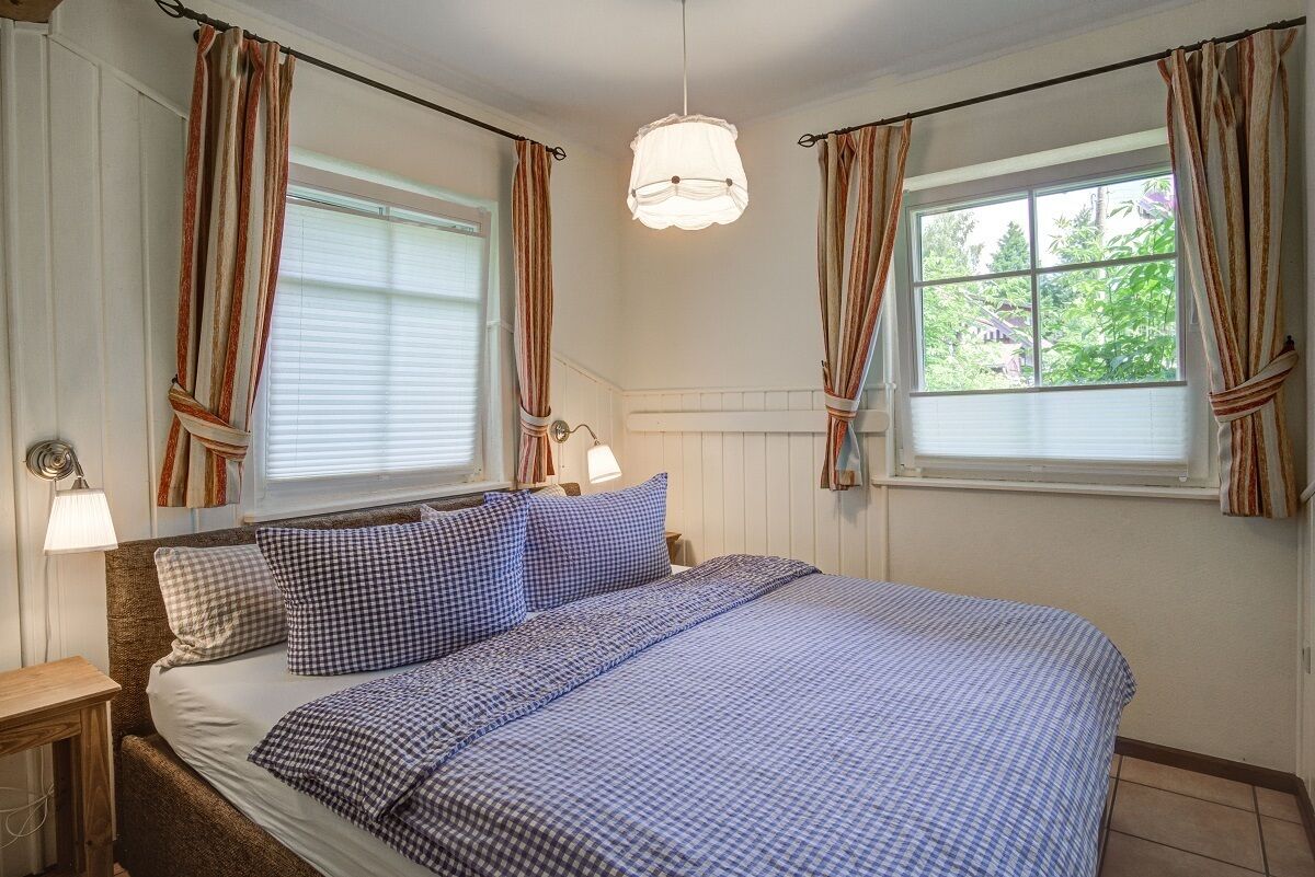 Ein Schlafzimmer mit einem Bett, zwei Nachttischlampen, einem Fenster mit Vorhängen und einer Pendelleuchte.