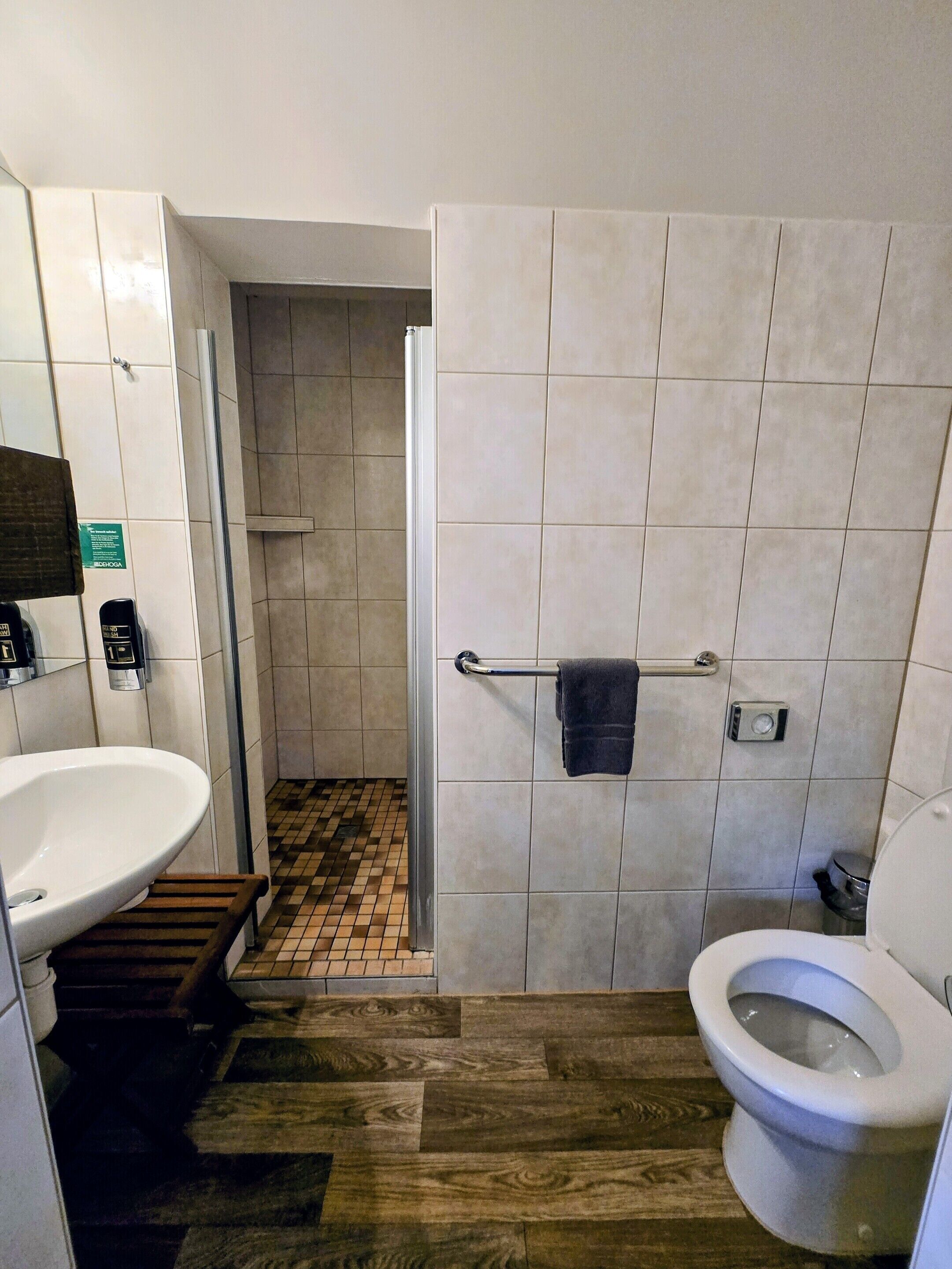 Ein Badezimmer mit weißem Waschbecken, Toilette, Duschbereich und Holzboden.