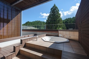 A hot tub area with steps leading up to it, a wooden deck, and a view of trees and sky.