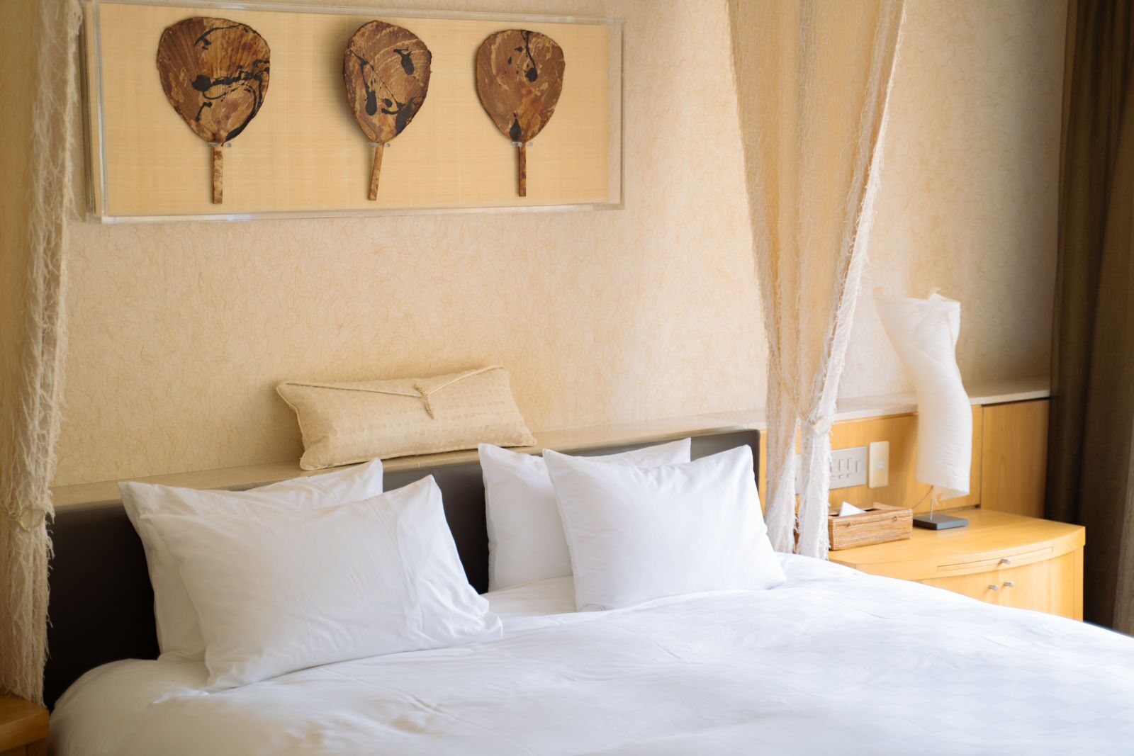 Ein Hotelzimmer mit Bett, Kissen, einem Nachttisch, einer Lampe und Wandbildern.