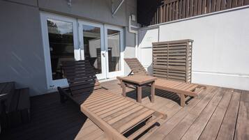 An outdoor deck with wooden furniture, including a table and chairs, and a sliding glass door leading to an interior space.