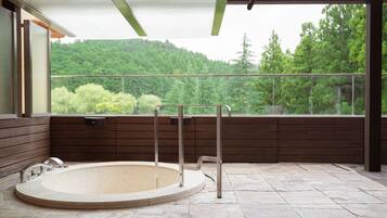 Un área de spa con un jacuzzi, paneles de madera y vistas a una ladera boscosa.