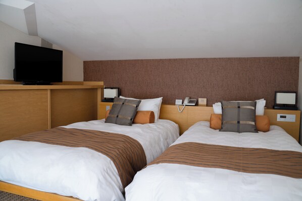 A hotel room with two beds, a television on a stand, and a headboard with a phone and a digital clock.