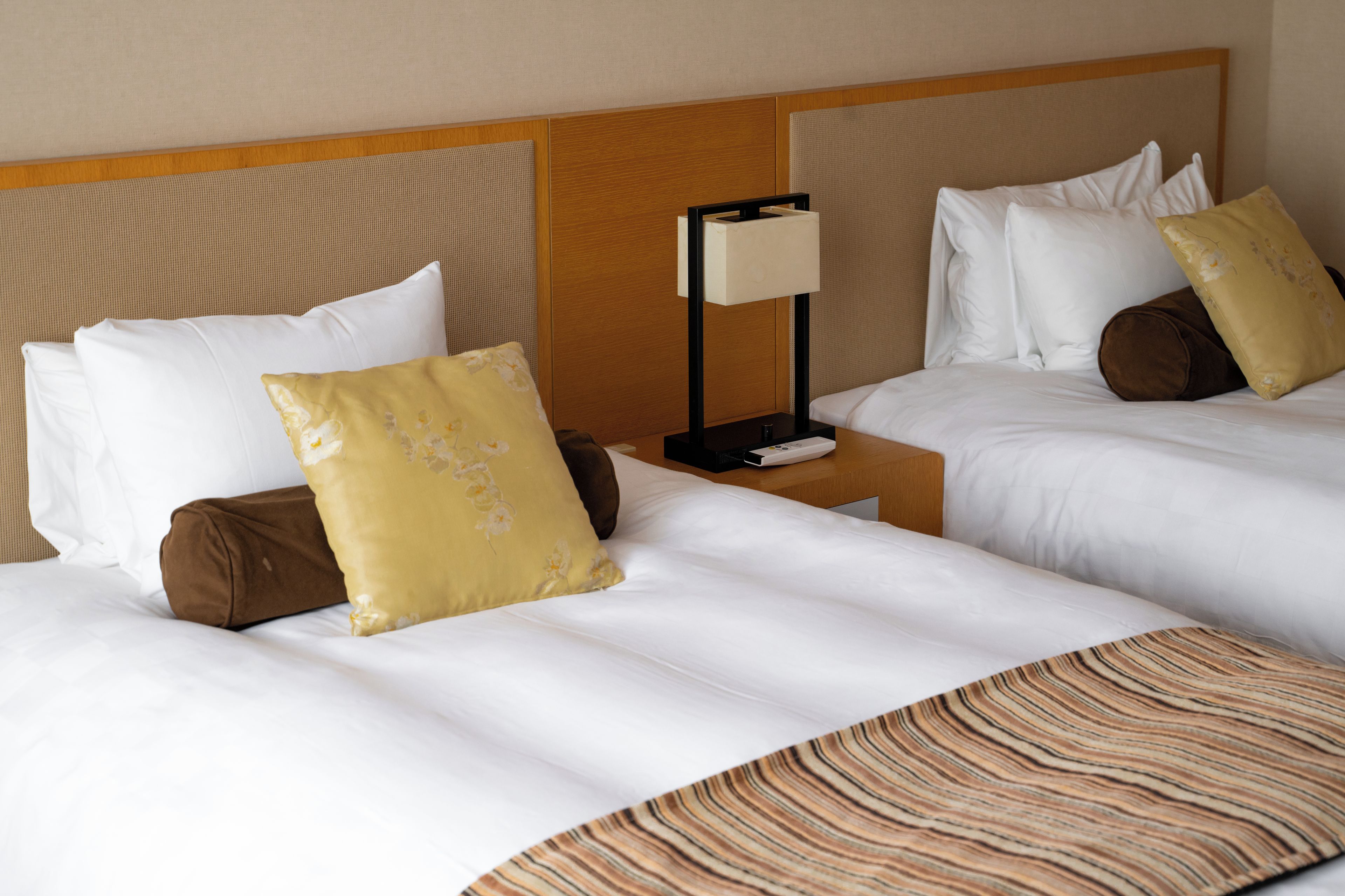 A hotel room with two beds, each with white bedding and decorative pillows. There is a nightstand with a lamp between the beds.