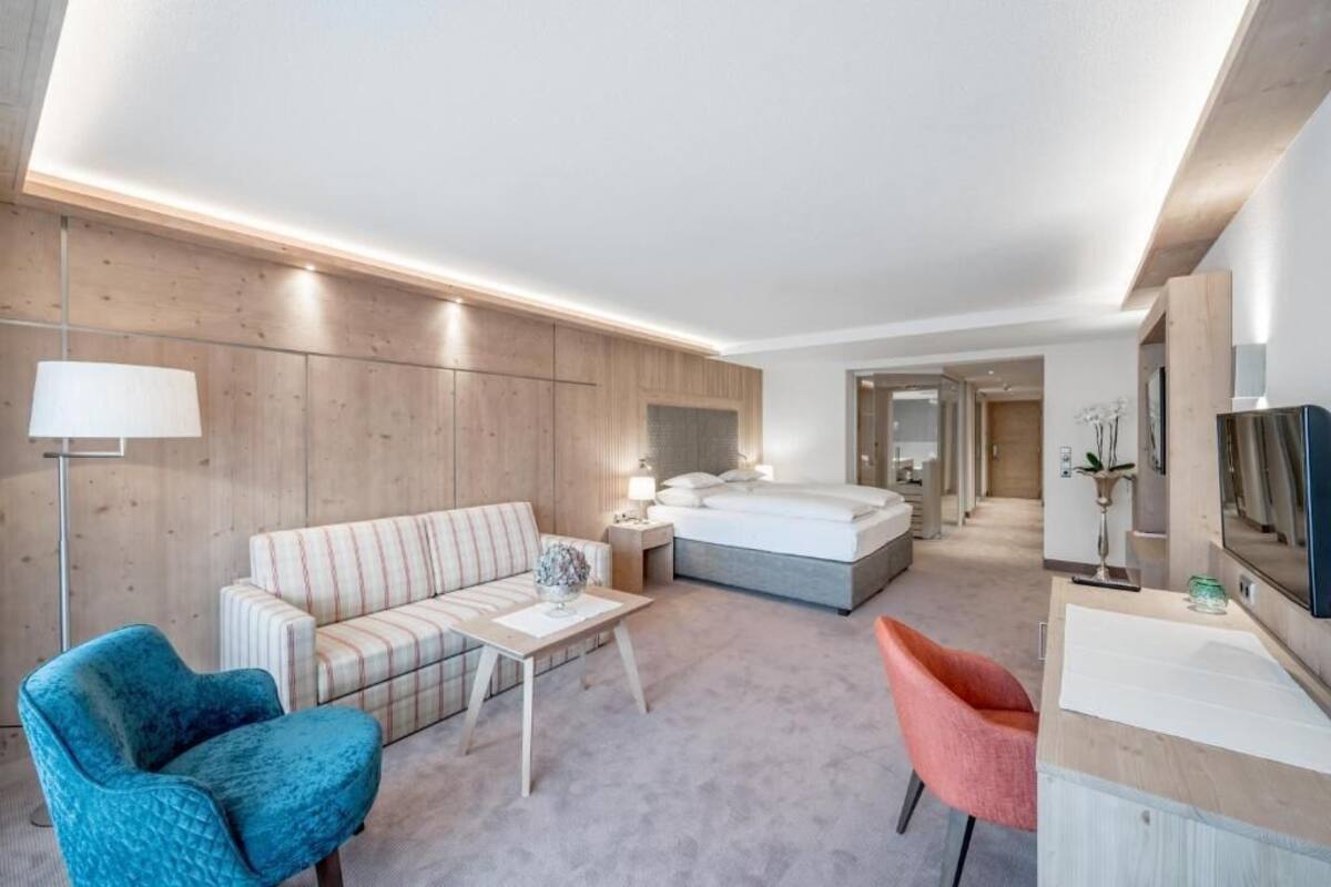 A modern hotel room with a bed, a sofa, a desk, and a TV.