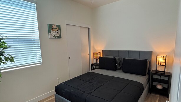 A bedroom with a bed, a ceiling fan, bedside lamps, a door, and a window with blinds. - Enjoyable 1-bedroom condo in Downtown Phoenix with Private garage (Phoenix)