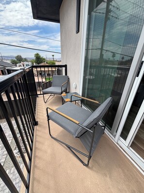 A balcony with two chairs and a table, a glass door, and a view of a residential area. - Enjoyable 1-bedroom condo in Downtown Phoenix with Private garage (Phoenix)