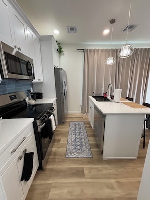 A modern kitchen with white cabinetry, a central island, stainless steel appliances, and a patterned rug. - Enjoyable 1-bedroom condo in Downtown Phoenix with Private garage (Phoenix)