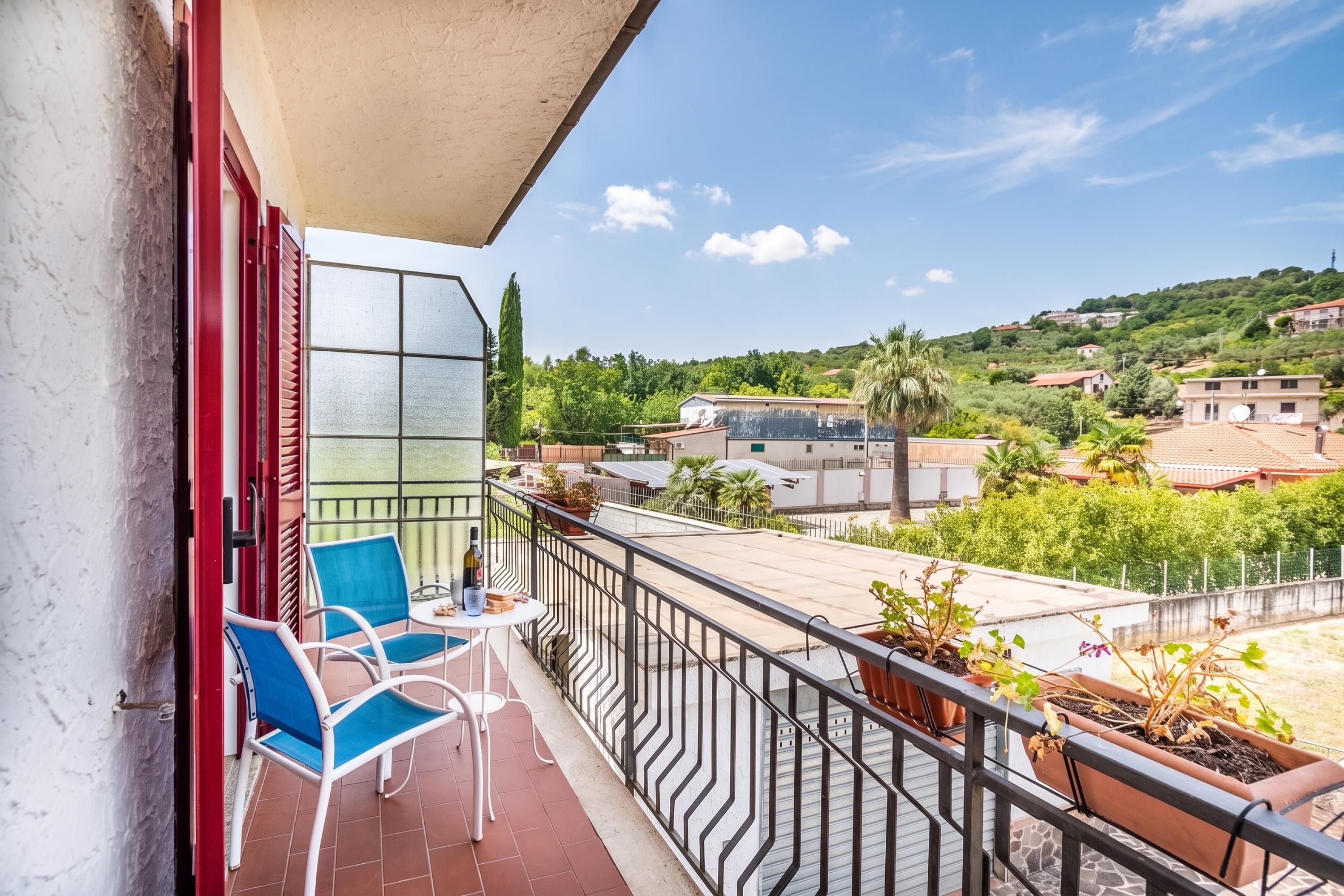 Een balkon met een tafel, stoelen en bloempotten.