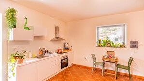 Una cocina compacta con armarios blancos, una estufa y una ventana con vistas a una casa.