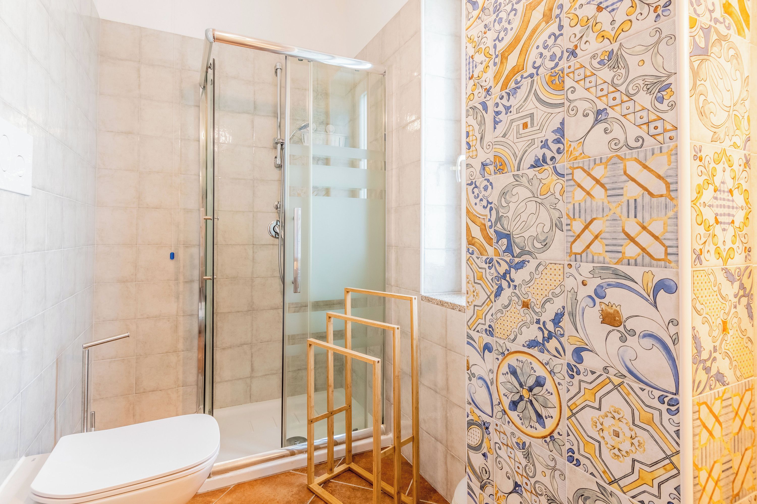 A bathroom with a glass shower enclosure, a toilet, and a tiled wall with a decorative pattern.