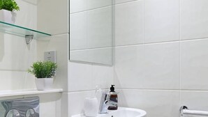 Ein Badezimmer mit einem weißen Waschbecken, einer Glasablage mit einer Pflanze, einem Handtuchhalter und einem Spiegel.
