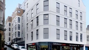 Ein mehrstöckiges Gebäude mit Hauseingang an einer Ecke, mit einem Geschäft namens 'Sainsbury's Local' im Erdgeschoss.