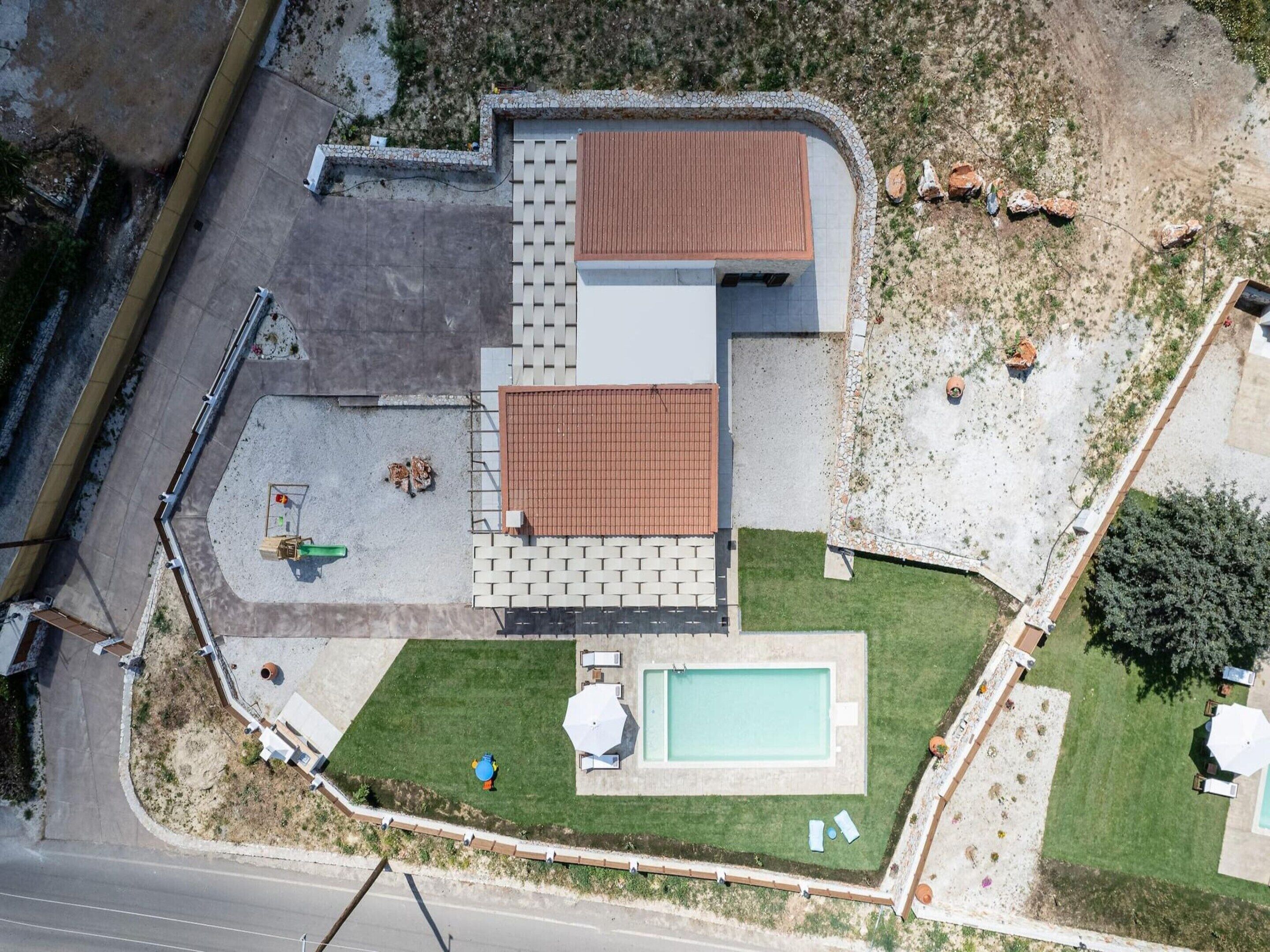 Vista aérea de una propiedad residencial con piscina, patio y jardín pequeño.