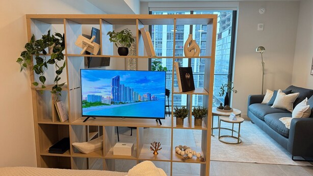 Ein modernes Wohnzimmer mit Fernseher, einer Couch, einem Couchtisch und einem Bücherregal mit Pflanzen und Dekorationselementen.