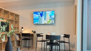 Ein modernes Wohnzimmer mit einem runden Esstisch, schwarzen Stühlen, einem B ücherregal, einem Fernseher an der Wand und einem großen Fenster.