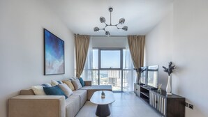 Een moderne woonkamer met een modulaire bank, een ronde salontafel, een televisie op een kast en een groot raam met gordijnen.