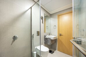 Ein modernes Badezimmer mit einer Duschkabine aus Glas, einer Toilette, einem Waschbecken mit Marmorplatte und einer Holztür.