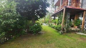 Un bâtiment en pierre doté d’un balcon, entouré d’une végétation luxuriante et d’une pelouse bien entretenue.