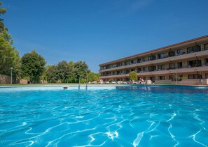 Ein Hotel mit Schwimmbad, mehreren Balkonen und blauem Himmel.