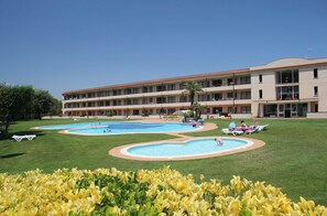 Ein Hotel mit mehreren Schwimmbecken, einem gepflegten Rasen und einem großen Gebäude mit Balkonen.