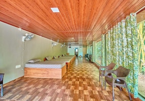 Una habitación con techo de madera, suelo a cuadros, una cama con colcha estampada y una fila de sillas a lo largo de una pared con cortina de bambú.
