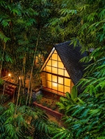Una pequeña casa rodeada de un denso bosque de bambú de noche.
