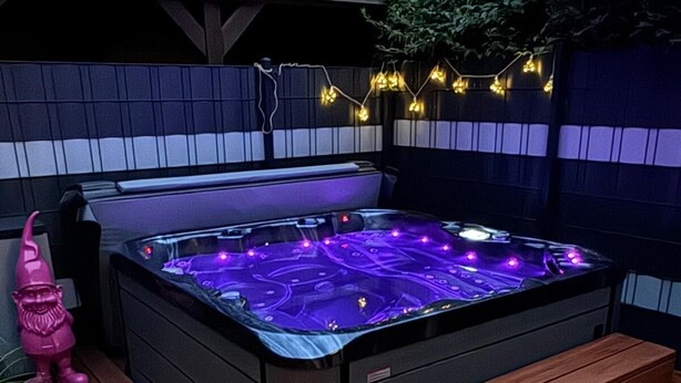 Ein Whirlpool mit einer Holzterrasse, einer Sitzbank und Lichterketten.