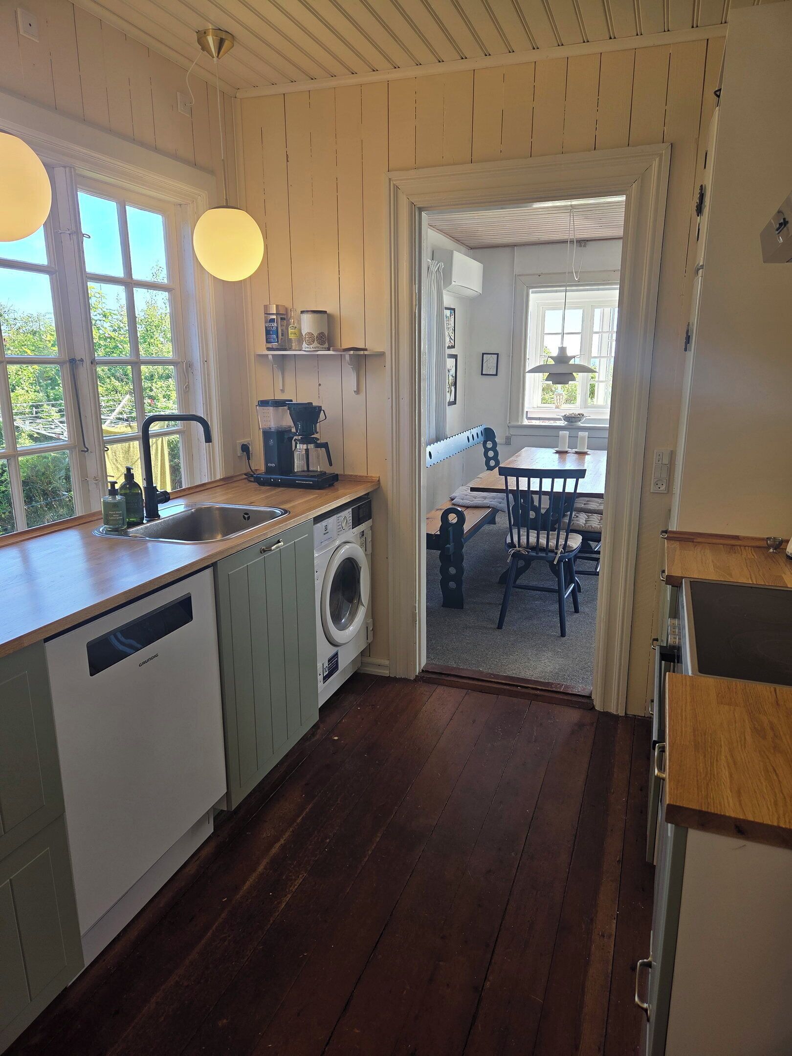 Une cuisine dotée de meubles en bois, d’un lave-vaisselle, d’une machine à café et d’un coin repas avec une table et des chaises.