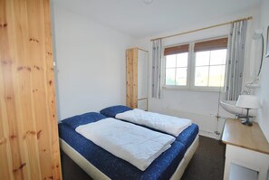 A room with two beds, a window with curtains, a radiator, and a wooden desk with a lamp. - Luxury Beach Villa in Makkum With Sauna (Makkum)