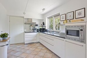 A modern kitchen with white cabinetry, a built-in microwave, and a window with a view of greenery. - Luxury Beach Villa in Makkum With Sauna (Makkum)