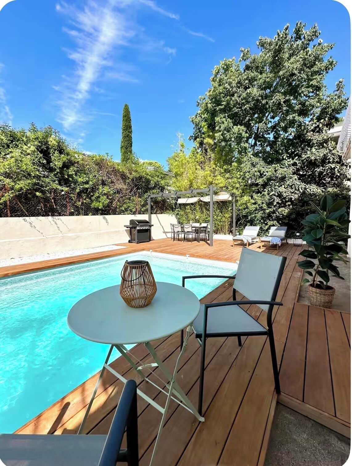 Une terrasse en bois avec une piscine, du mobilier d’extérieur et une pergola dotée de parasols.