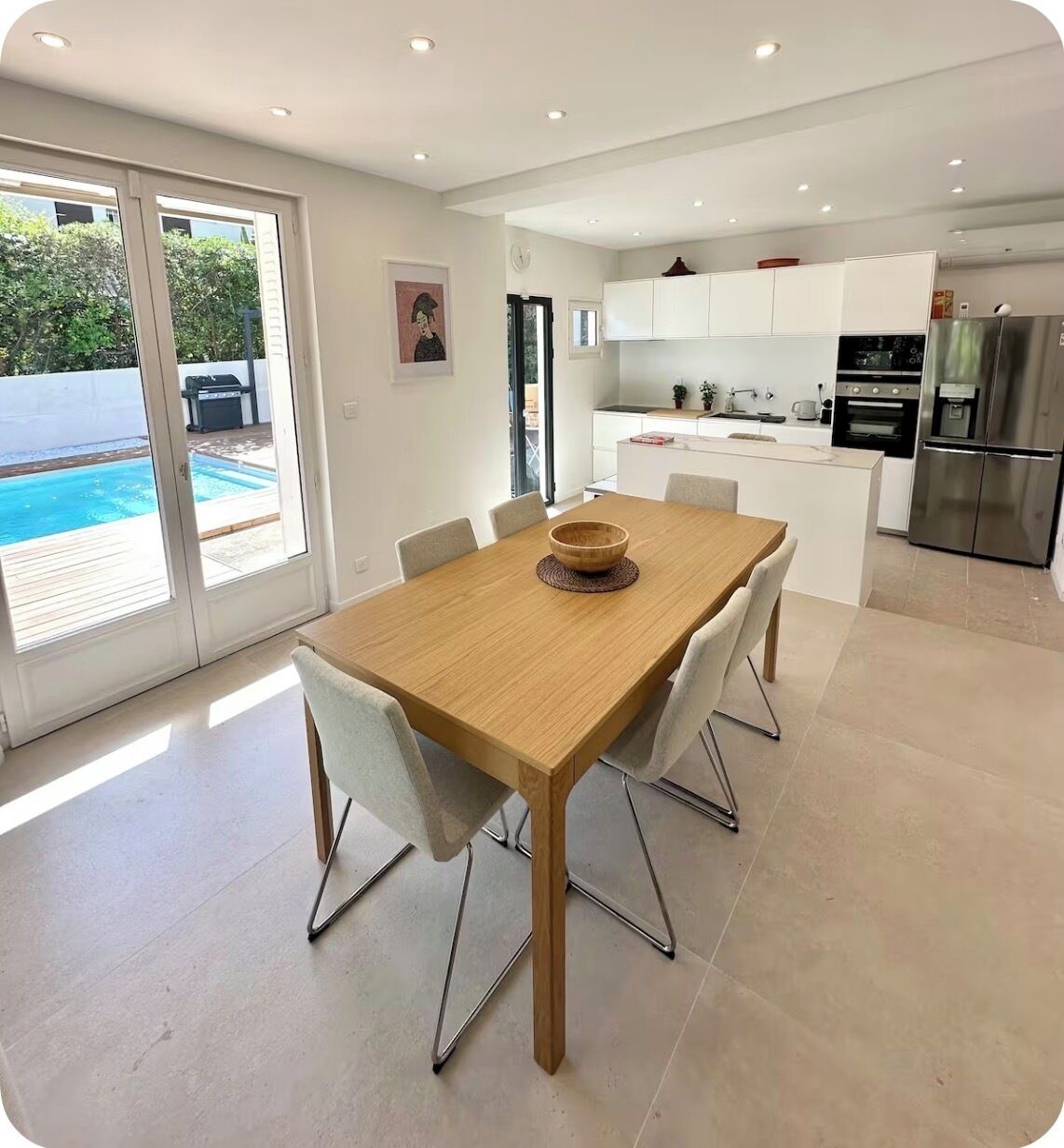 Une cuisine moderne avec des meubles blancs, des appareils en acier inoxydable et un coin repas comprenant une table et des chaises en bois.