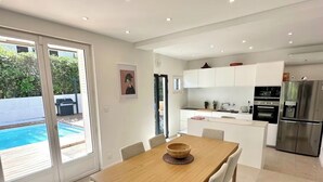 A modern kitchen with white cabinets, stainless steel appliances, and a dining area with a wooden table and chairs. - La Villa du Sud - Standing & Calme, 20mn Plages (100% climatisée) (Montpellier)
