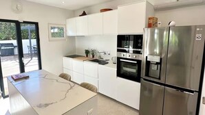 A modern kitchen with white cabinetry, a built-in oven, a stainless steel refrigerator, and a marble countertop island. - La Villa du Sud - Standing & Calme, 20mn Plages (100% climatisée) (Montpellier)