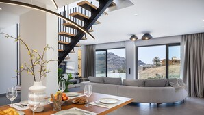 Uma zona de refeições moderna com uma mesa de madeira posta para uma refeição, uma escadaria e vista para uma paisagem montanhosa.