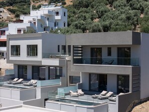 A modern multi-story building with balconies, a rooftop pool area, and a view of olive groves. - Maple Villa 1 Deluxe Sea View Villa in Walking Distance From Beach (Agios Vasileios)