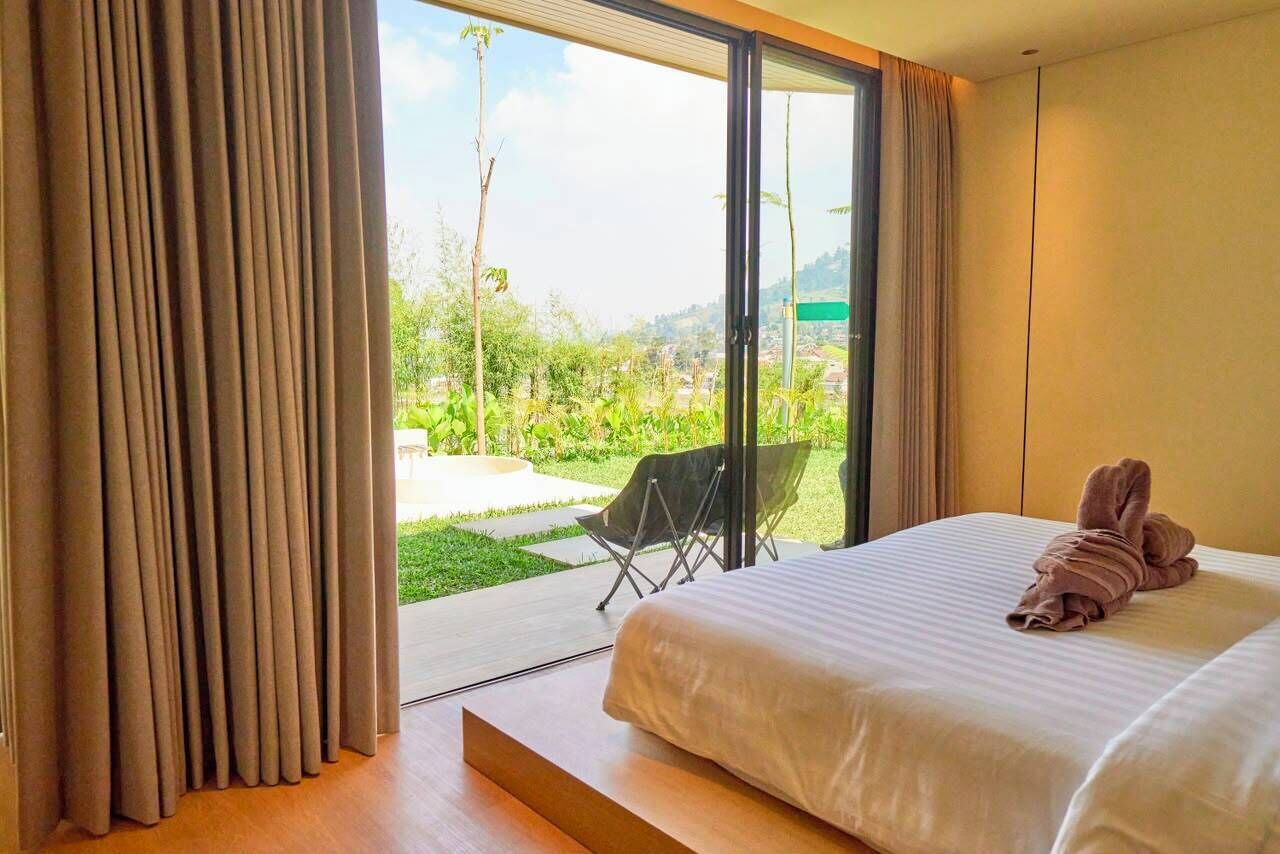 Un dormitorio con cama, una silla y vistas a un jardín y edificios.