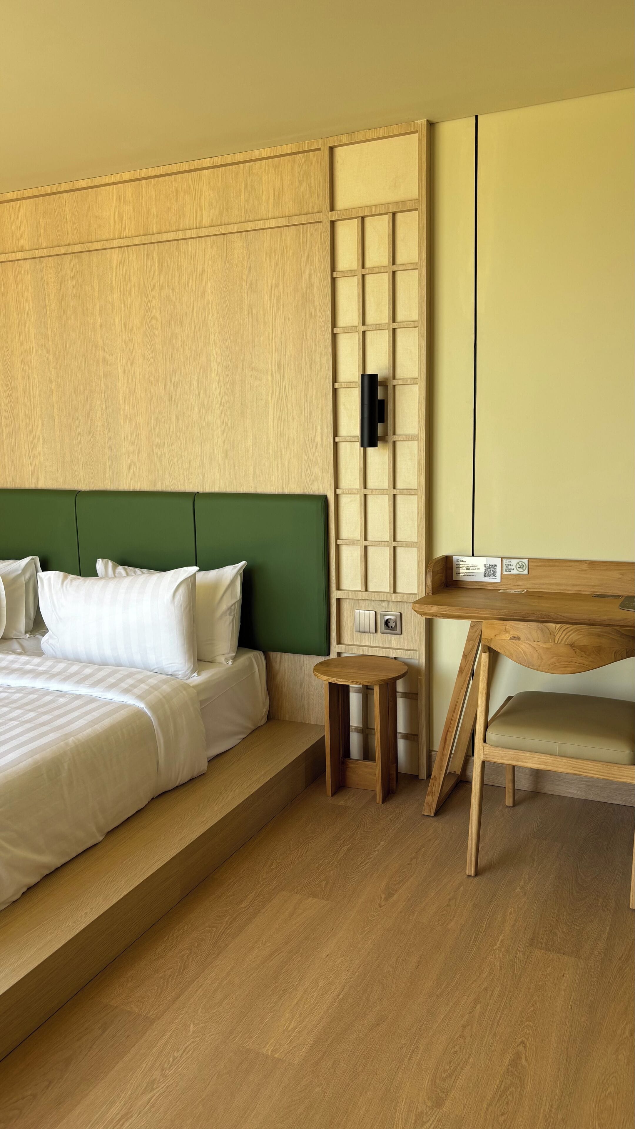 A hotel room with a bed, a small wooden table, a bench, and a wall panel.