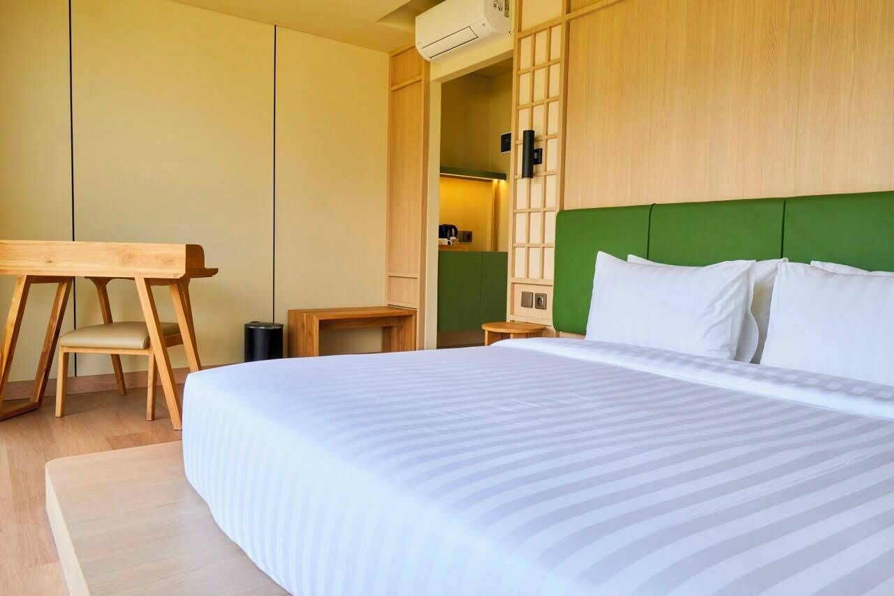 Habitación de hotel con cama, escritorio, silla y cabecera verde.