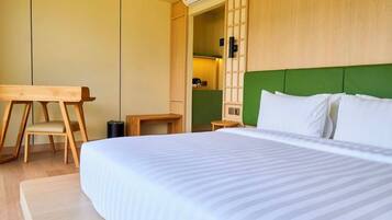 Habitación de hotel con cama, escritorio, silla y cabecera verde.