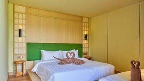 Quarto de hotel com cabeceira verde, duas camas e uma pequena mesa de madeira.