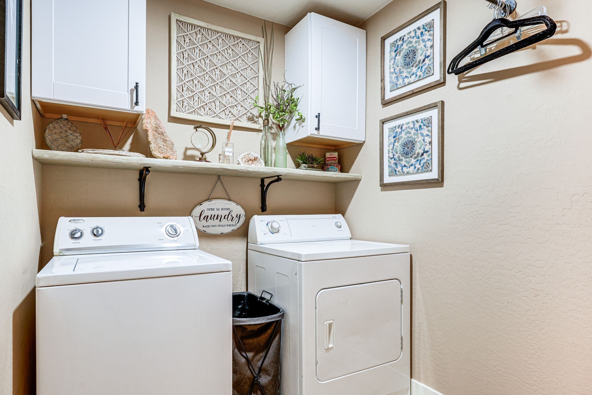 A laundry room with two washing machines, a drying rack, and a shelf with decorative items.