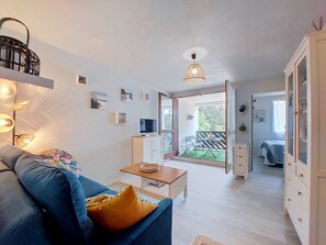 Ein modernes Wohnzimmer mit Sofa, Couchtisch, Fernseher und einem Balkon mit Gartenmöbeln.
