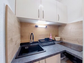 Eine Küche mit einem schwarzen Spülbecken, Holzschränken, einer Leuchte und einem Korb.